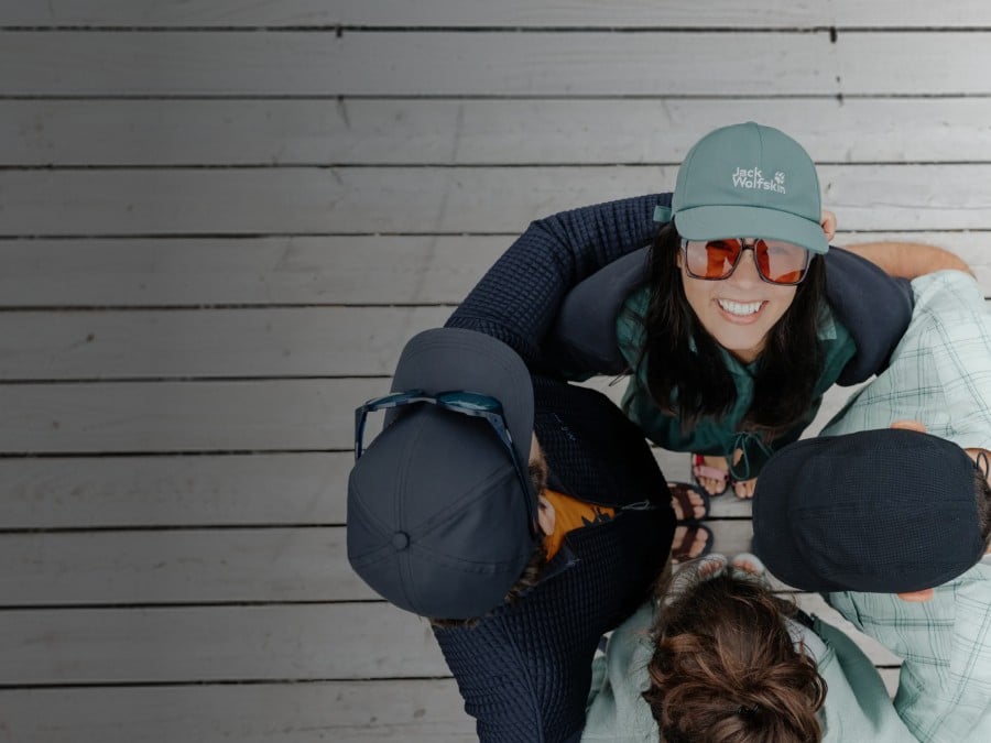 Two sleds with two people each are riding down a snowy slope. The people are laughing and wearing winter clothing, hats, and sunglasses; snow-covered mountains can be seen in the&nbsp;background.